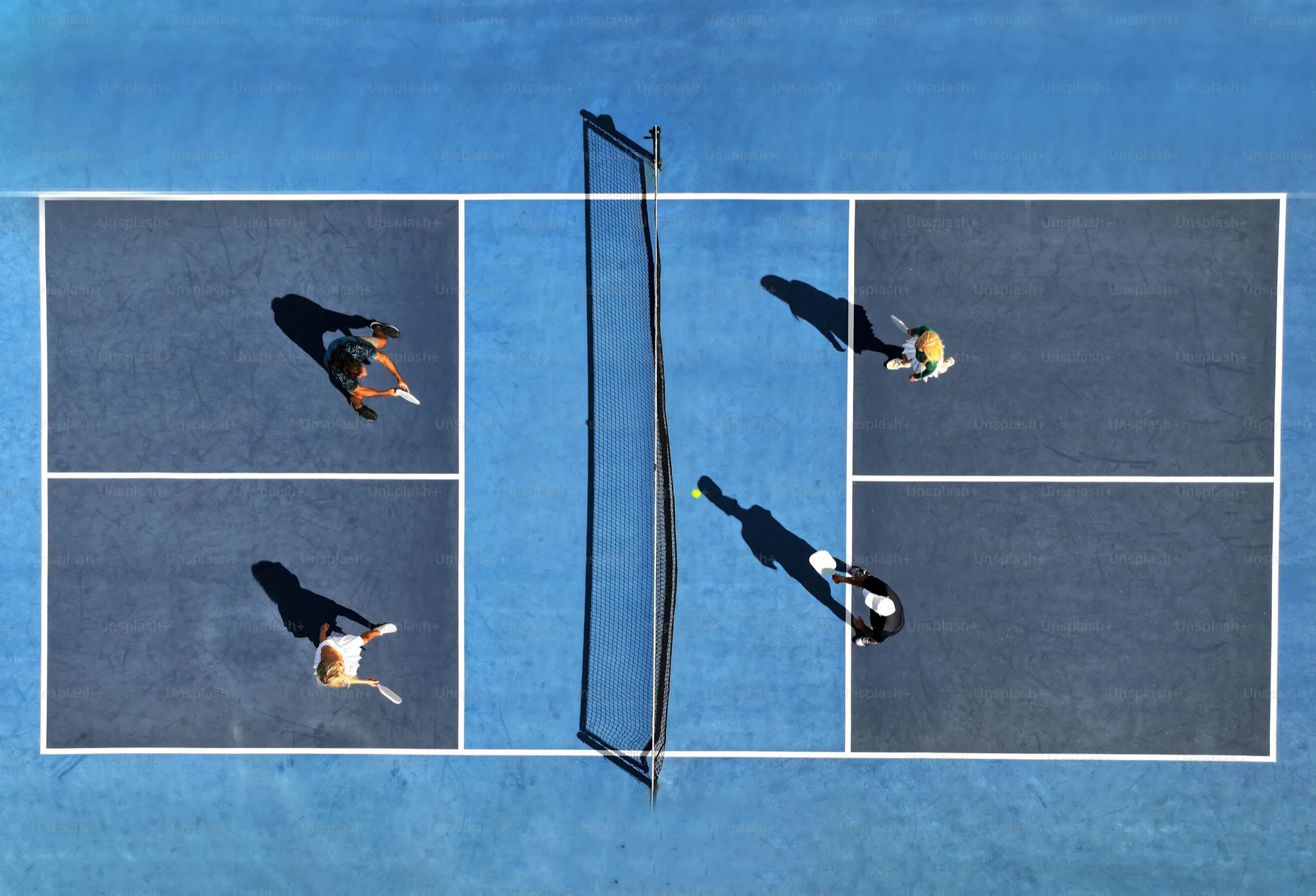 Aerial view of four people playing pickleball on a blue court with a net