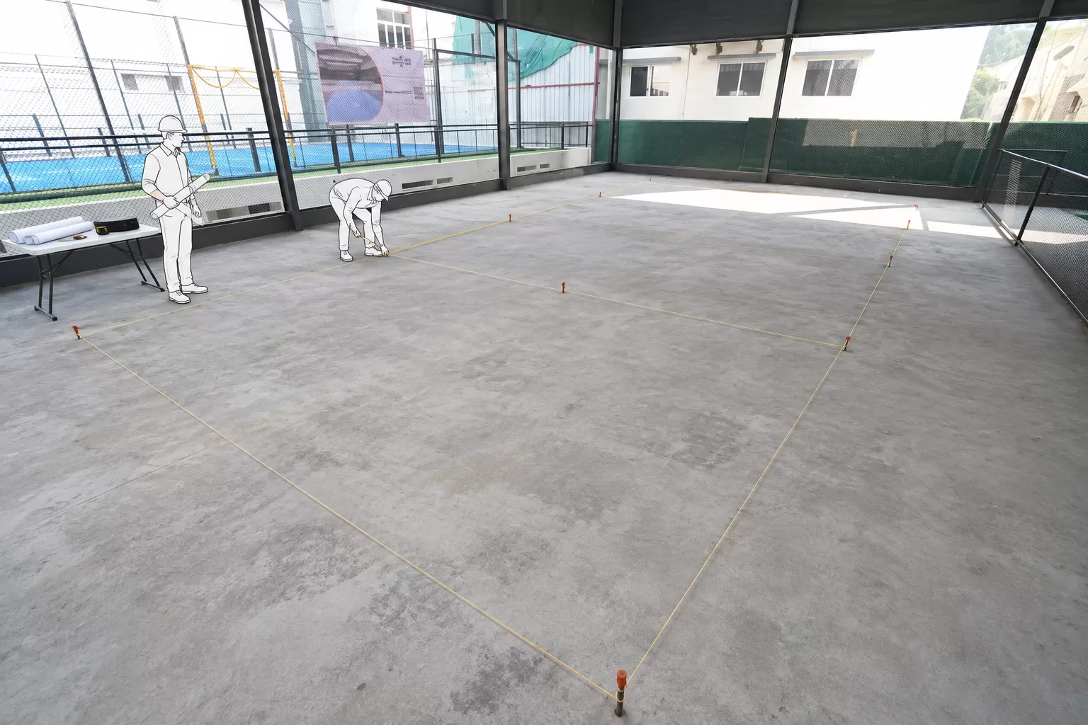 Two workers marking out the court layout with pegs and string on a bare concrete slab before a pickleball court is built